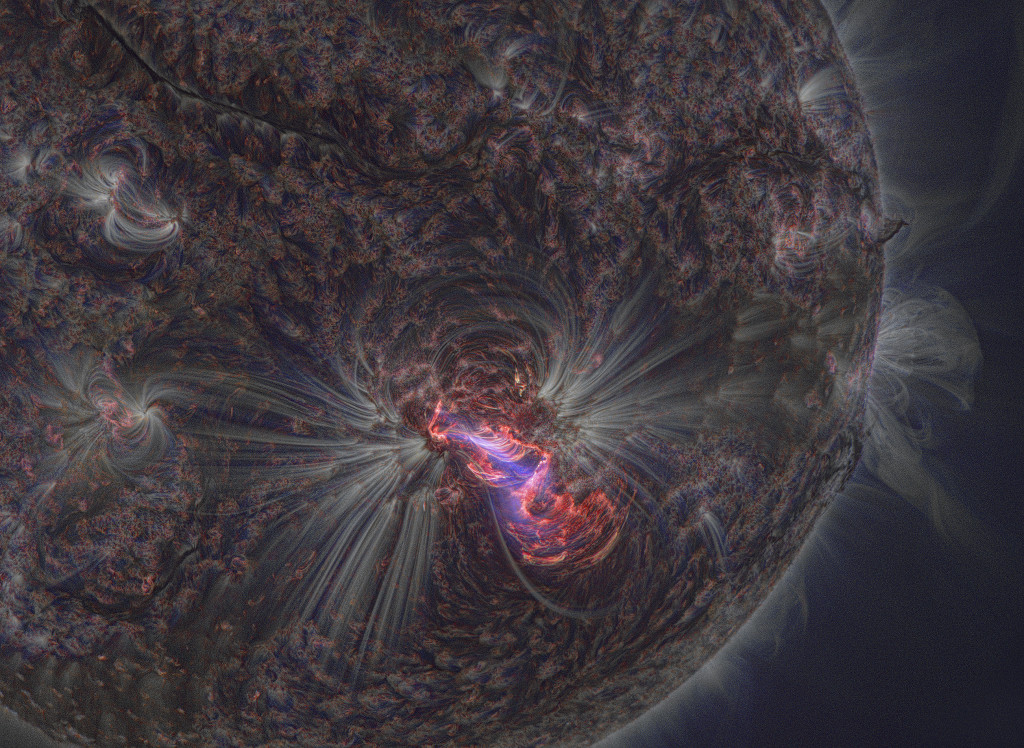 Die Sonne wirkt hier sehr dunkel. Aus ihrer Oberfläche dringen weißliche nebelige Strahlen, sie zeigen das Magnetfeld. In der Mitte leuchtet eine rot-violette aktive Region.