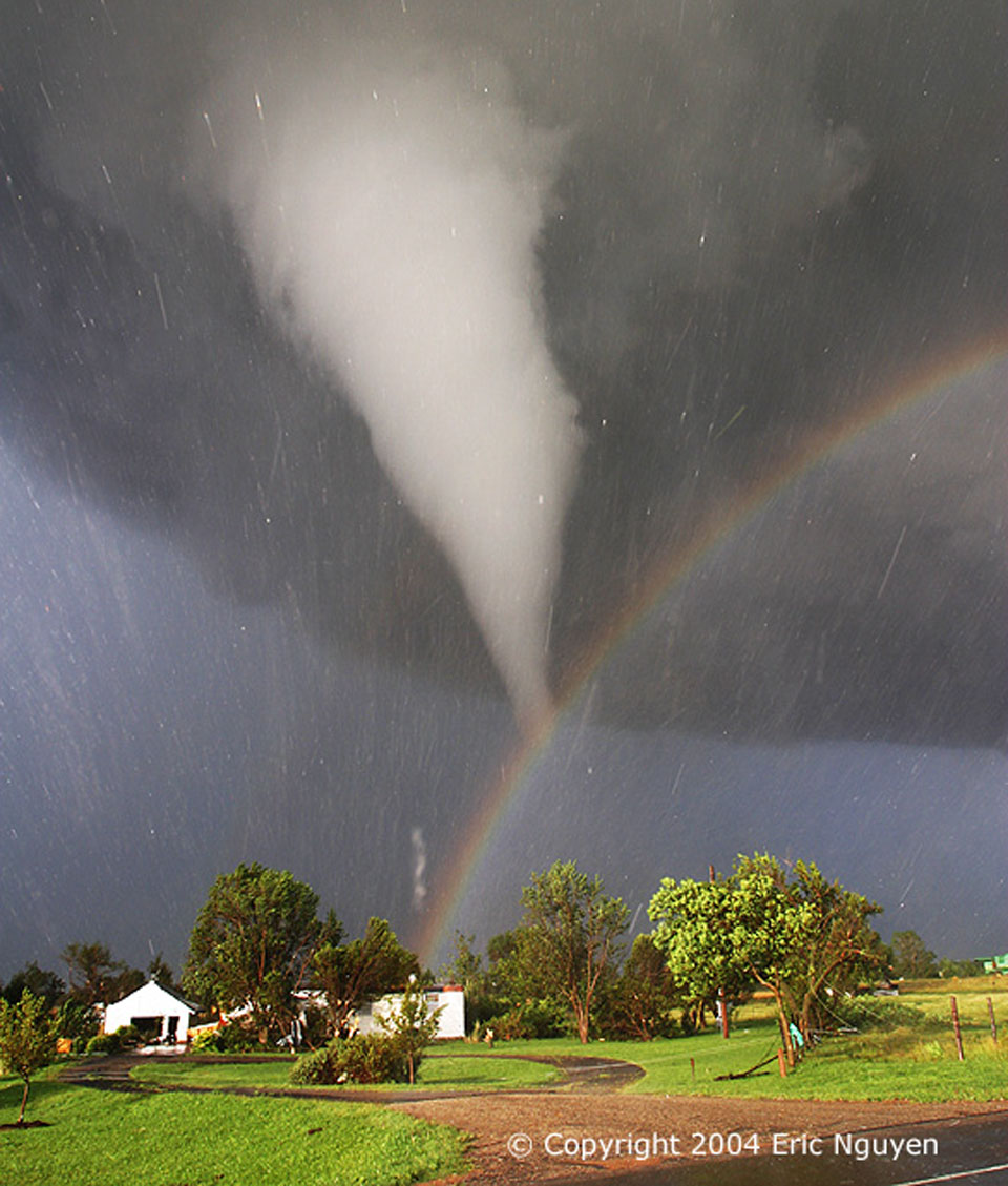 Das Bild wirkt friedlich, ist aber sehr stürmisch. Hinten hängt ein Tornadotrichter vom dunklen Wolkenhimmel, Hagel peitscht durchs Bild. Über der sonnenbeschienenen Szene leuchtet ein Regenbogen.