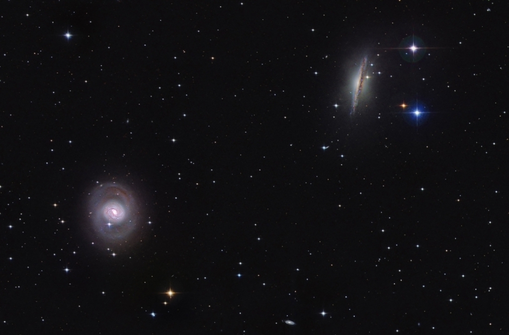Links unten ist die Spiralgalaxie M77 von oben zu sehen, rechts oben ist NGC 1055 von der Kante sichtbar. Beide Galaxien sind von wenigen Sternen und einigen Galaxien umgeben. Die Galaxien sind viel weiter entfernt als die beiden großen Galaxien.