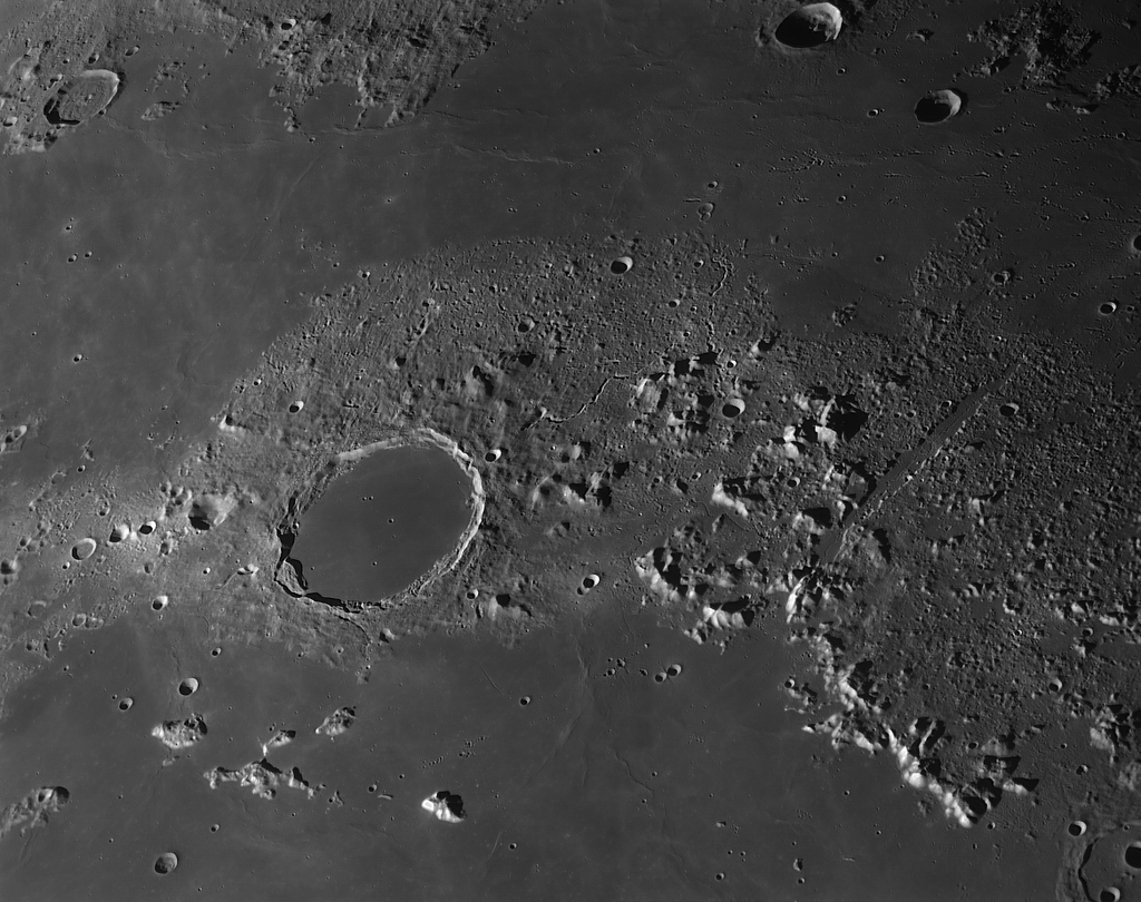 Mitten im Bild ist der Krater Plato mit seinem ausgeprägten Wall ein kreisförmiger Einschnitt in die Mondalpen, die rechts im Bild verlaufen. Oben ist eine glatte Ebene, das Regenmeer.