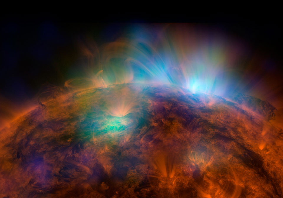 Die Sonne ist in energiereichem Ultraviolettlicht dargestellt. Aus der roten, gefaserten Oberfläche dringen blau und grün leuchtende Ausbrüche.