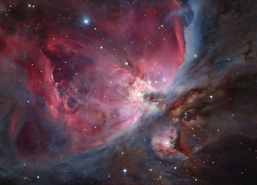 Der Orionnebel ist bildfüllend dargestellt. Nach links oben öffnet sich eine magenta-fliederfarbene Höhlung, die links und unten in grauviolette Nebel gehüllt ist. In der Mitte leuchten die Trapezsterne. Rechts unten sind dunkle Molekülwolken und ein kleiner, kugelförmiger rosaroter Nebel mit einem hellen Stern in der Mitte.