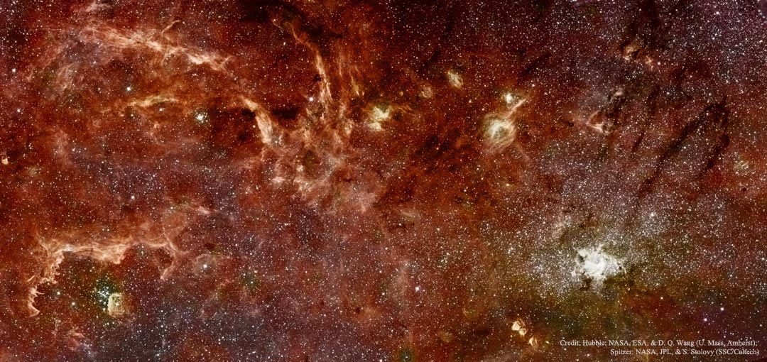 Das Bild ist rötlich und voller Nebel und Sterne. Es zeigt die dichte Umgebung im Zentrum der Galaxis in Infrarot-Wellenlängen.