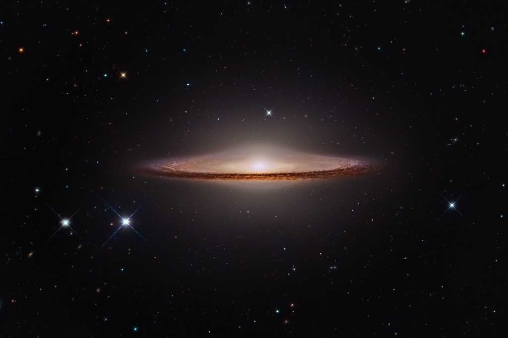 Mitten im Bild schwebt eine Spiralgalaxie, die hier an ein Ufo erinnert. Über einem hellen Kern wölbt sich eine nebelige Kuppel, die an Glas erinnert, außen herum verläuft ein breiter, sehr markanter Staubring.