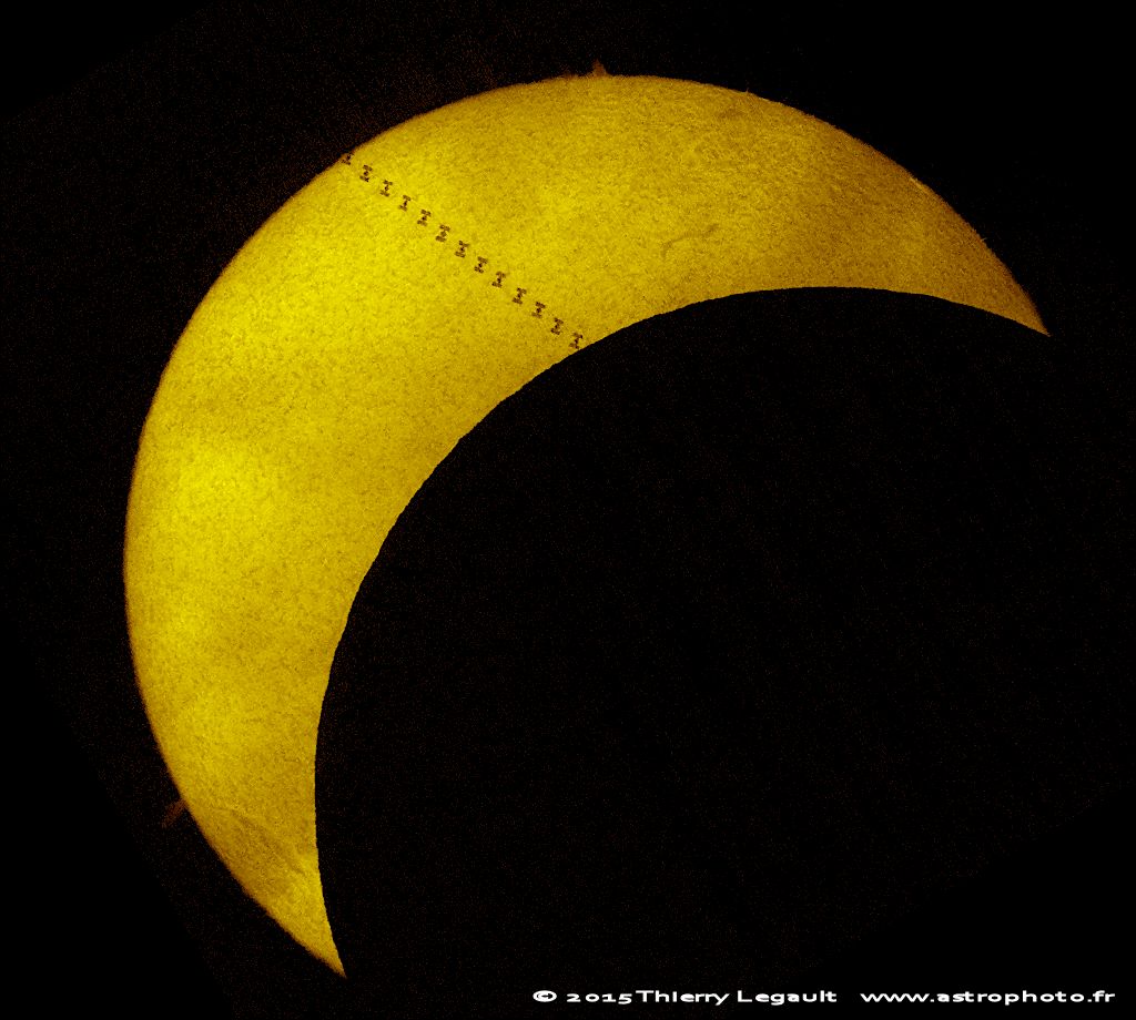 Die Sonne wird vom Mond und von der Internationalen Raumstation verdeckt. Auf der Oberfläche ist die Granulation erkennbar, außerdem Filamente und am Rand Protuberanzen.