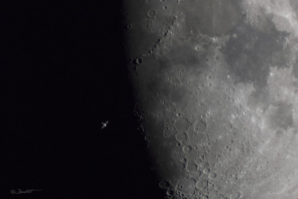 Mitten durchs Bild verläuft die Grenze zwischen Tag und Nacht auf dem Mond, der sogenannte Terminator. An dieser Grenze sind Krater besonders gut erkennbar. Vor der dunklen Nachtseite leuchtet die winzige Internationale Raumstation ISS.