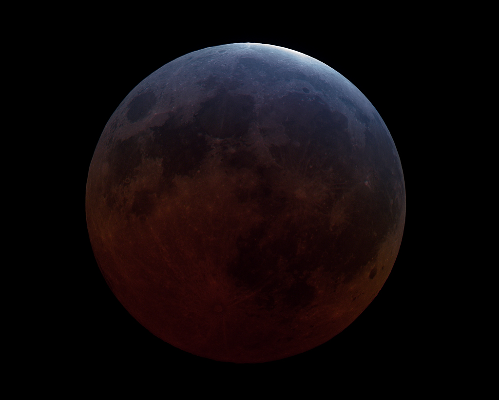 Der Vollmond ist merkwürdig dunkel, weil er in den rötlichen Schatten der Erde getaucht ist. Nur oben schimmert er hell und bläulich, denn dorthin fällt Sonnenlicht, das von der oberen Ozonschicht der Erde gefiltert wird.