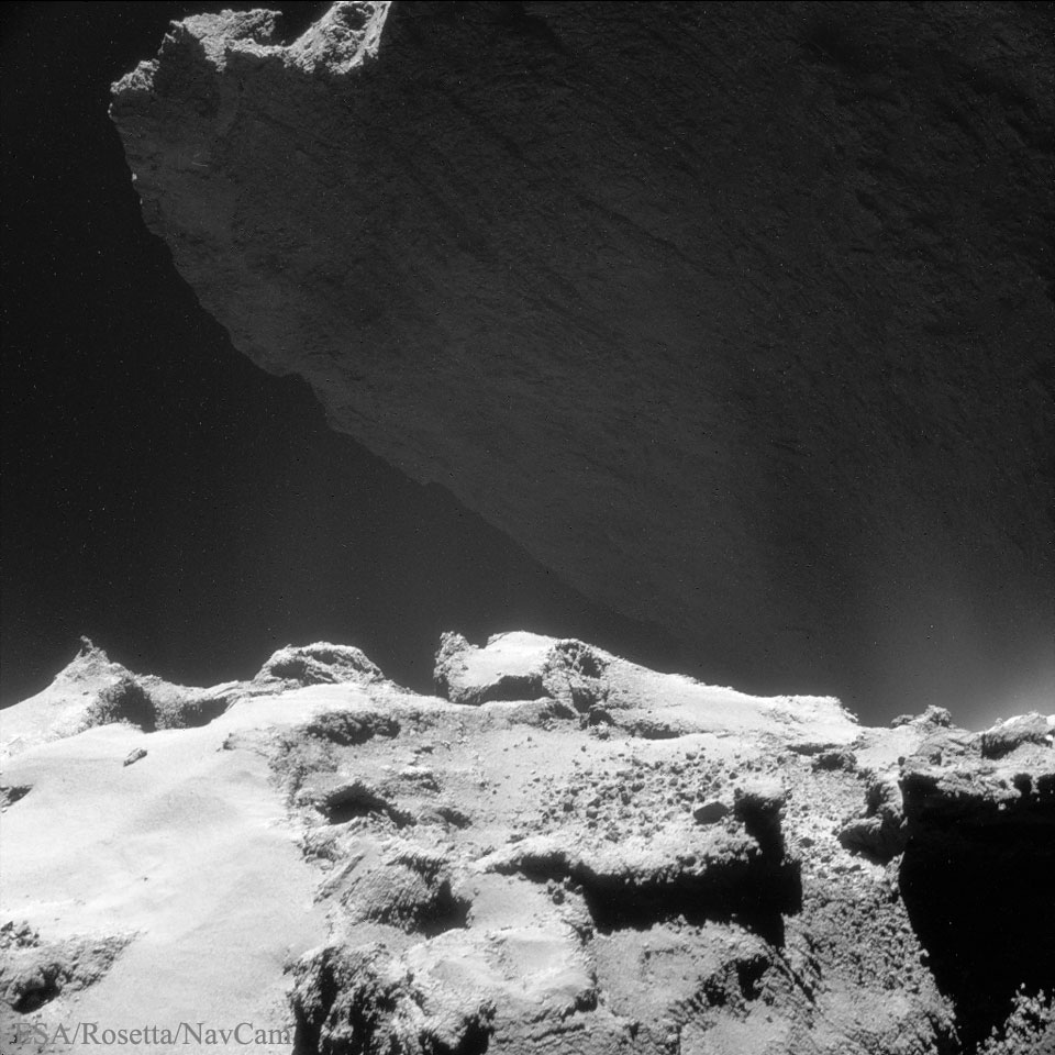 Über einem sonnenbeschienenen Haufen mit Geröll ragt eine schattige Klippe hoch. Es ist der Komet Tschurjumow-Gerassimenko, das Bild stammt von der Raumsonde Rosetta.