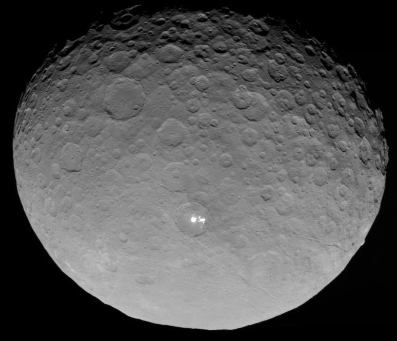 Der Zwergplanet Ceres ist fast bildfüllend dargestellt. Oben ist die Schattenlinie zur Nacht, an der Krater besonders plastisch hervortreten. In der Mitte leuchten helle Flecken in einem größeren Krater.