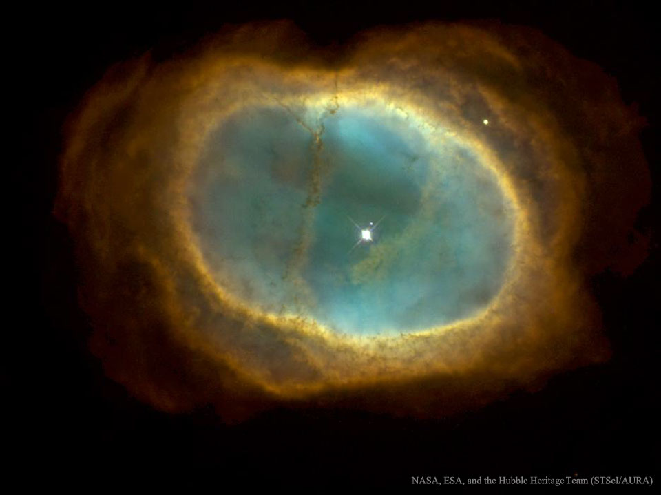Ein ovaler, ockergelber Ring ist mit einem mattblau leuchtenden Lichtsee gefüllt. Im Inneren ist ein heller Stern, der schwache Stern daneben erzeugte den planetarischen Nebel.