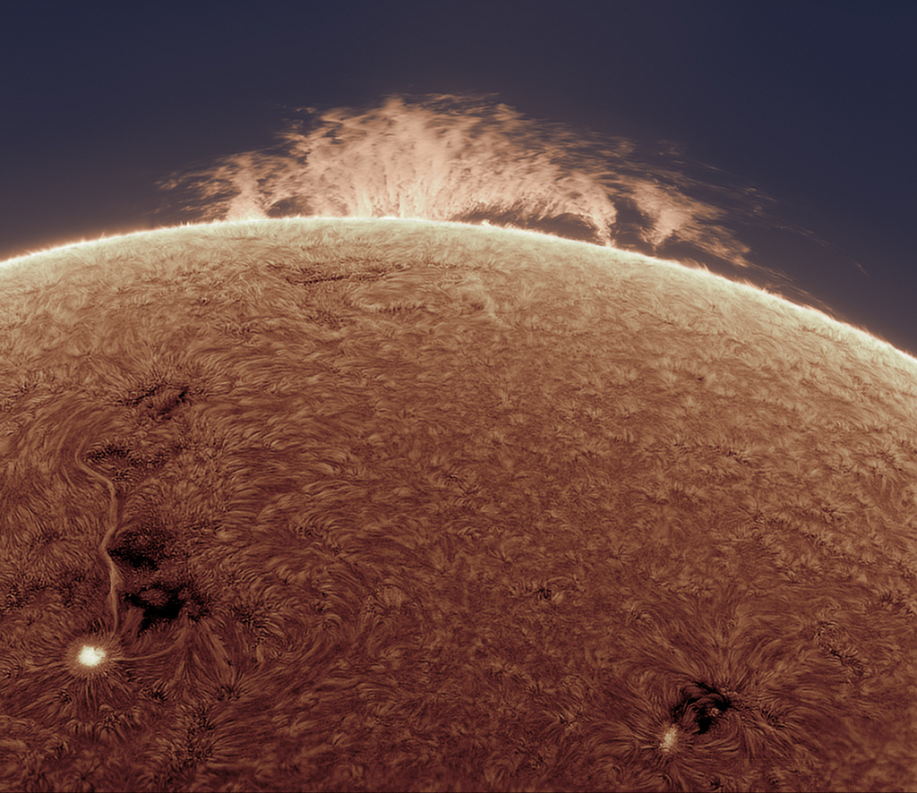Die Sonne ist teilweise invertiert dargestellt. Sonnenflecken und der Sonnenrand sind hell. Auf Bildern in sichtbarem Licht sind diese Merkmale dunkler. Über dem Horizont schwebt eine riesige Sonnenfackel, die sogar größer ist als der Planet Jupiter.