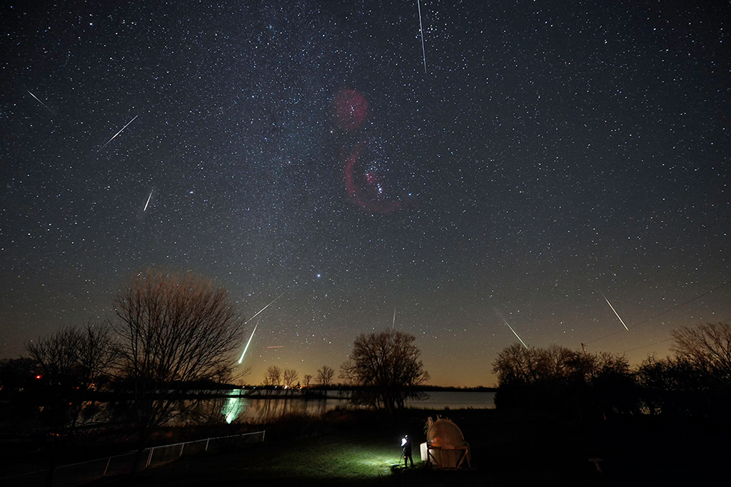 Am Himmel über einer Gartensternwarte in Onrario fallen Meteore vom Himmel. Dort leuchtet das Sternbild Orion mit der Barnardschleife und ganz oben der Sternhaufen der Hyaden.