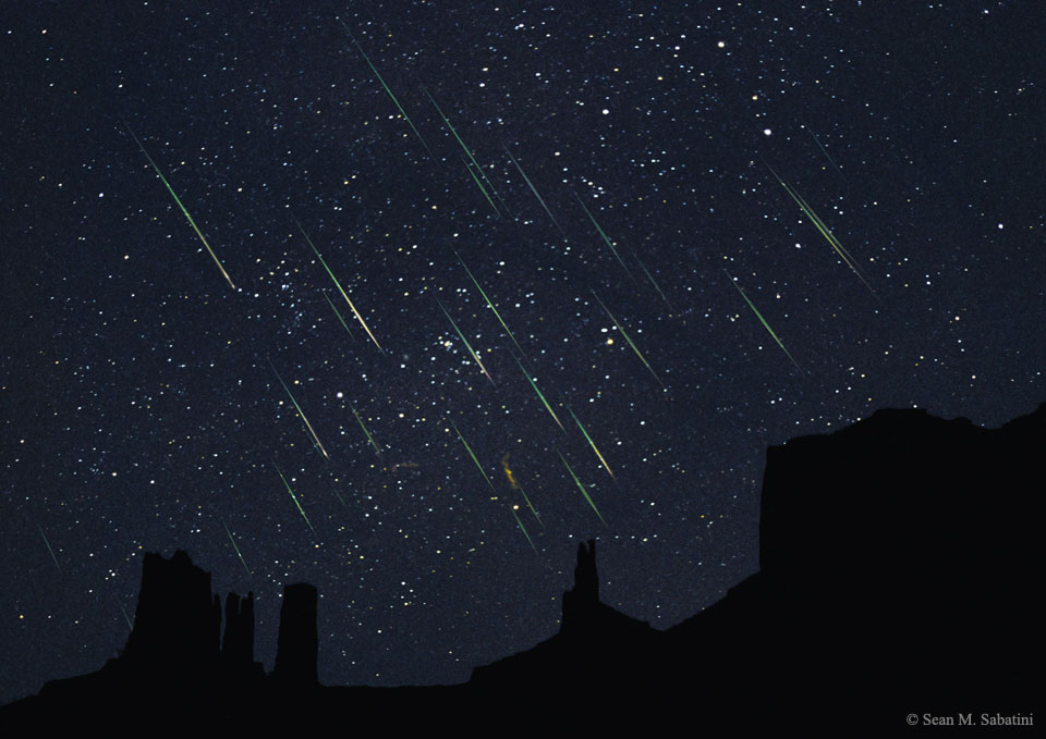 Wie Regen strömen Meteore der Leoniden vom sternklaren Himmel. Vorne zeichnen sich die Silhouetten der Tafelberge im Monument Valley ab.