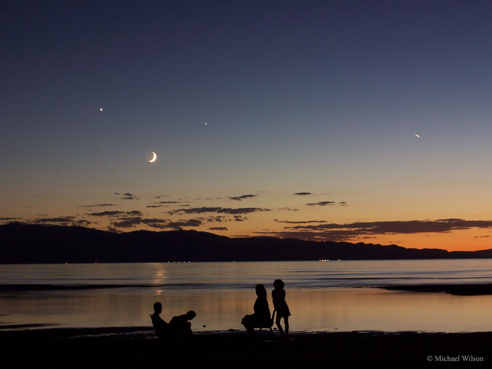 Am Ufer des Großen Salzsees bewundern vier Personen den Himmel in der Dämmerung mit Mond, Planeten und dem hellen Stern Spica.