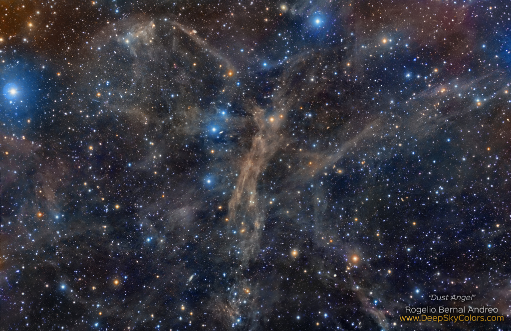 Faserartige Staubwolken durchziehen das Sternenfeld. Einige Sterne sind von blau leuchtenden Nebeln umgeben.