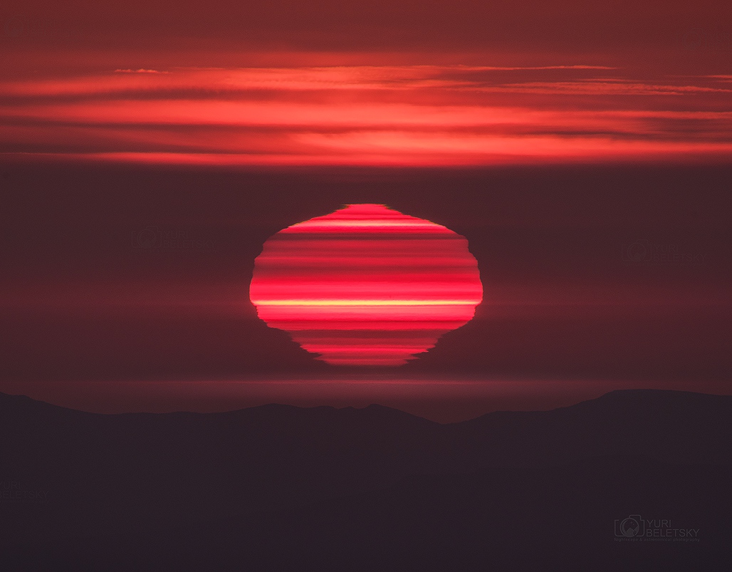 Hinter dunklen Wolken geht die Sonne unter, sie ist dicht gestreift und vertikal verzerrt.