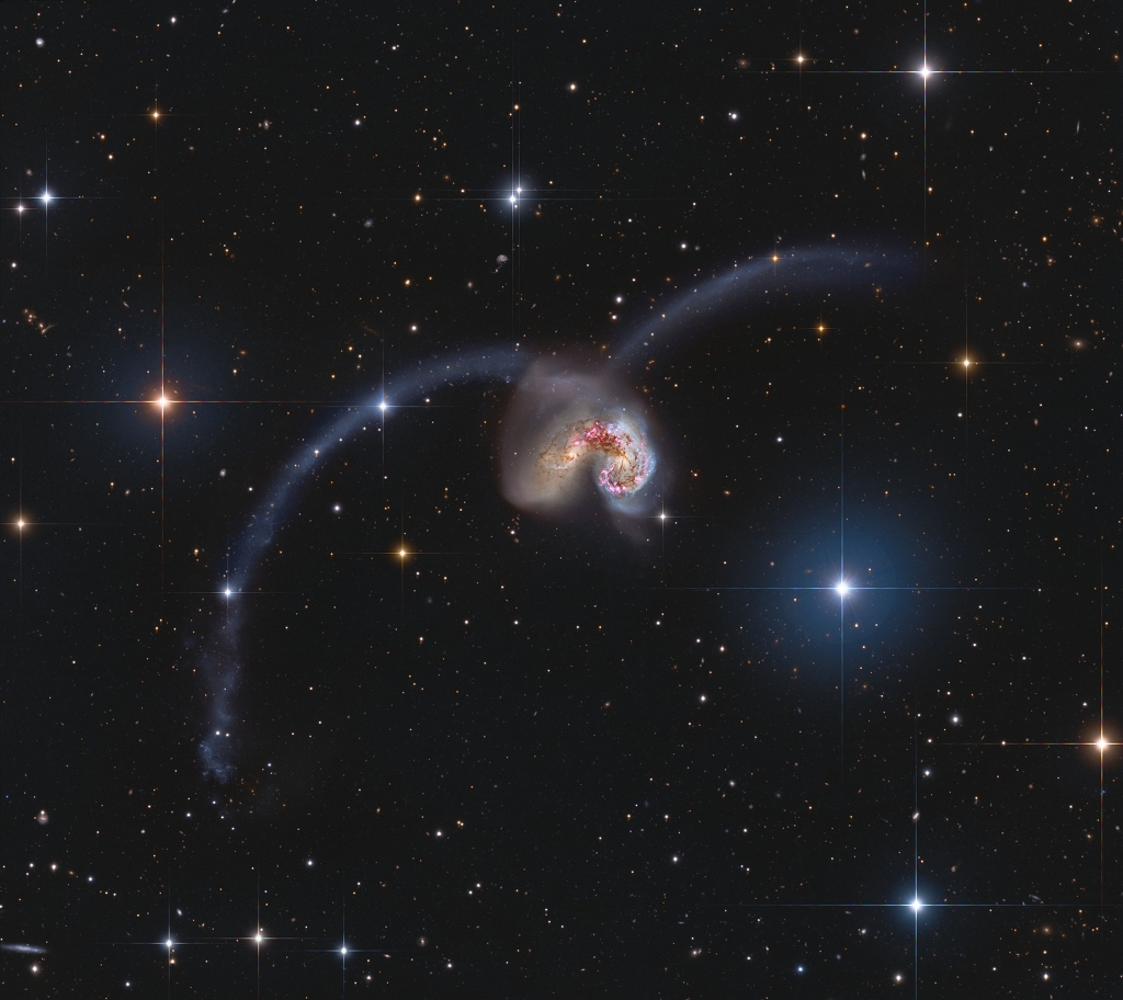 Hinter lose verteilten Sternen, von denen einige wenige hell leuchten, sind zwei verzerrte Galaxien angeordnet, die miteinander wechselwirken. Zwei Sternströme sind in großen Bögen hinausgeschleudert.