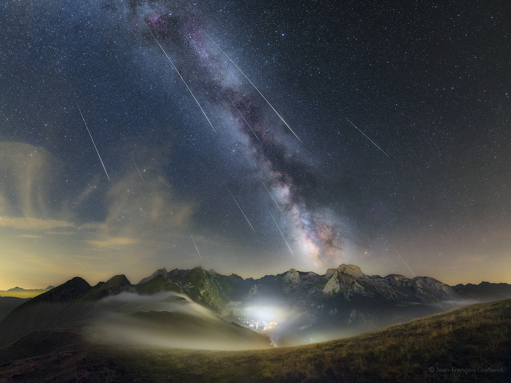 Über den nebelverhangenen Berggipfeln in den Pyrenäen steigt schräg die Milchstraße auf, vom Himmel blitzen Leuchtspuren von Meteoren der Perseïden.