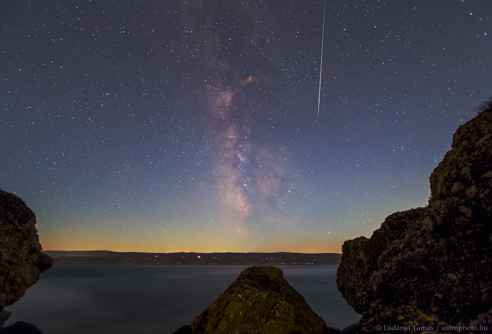 Hinter dem Meer liegt die Insel Brač an der dalmatinischen Küste. Darüber steigt die Milchstraße senkrecht auf, vom Himmel fällt ein Meteor.