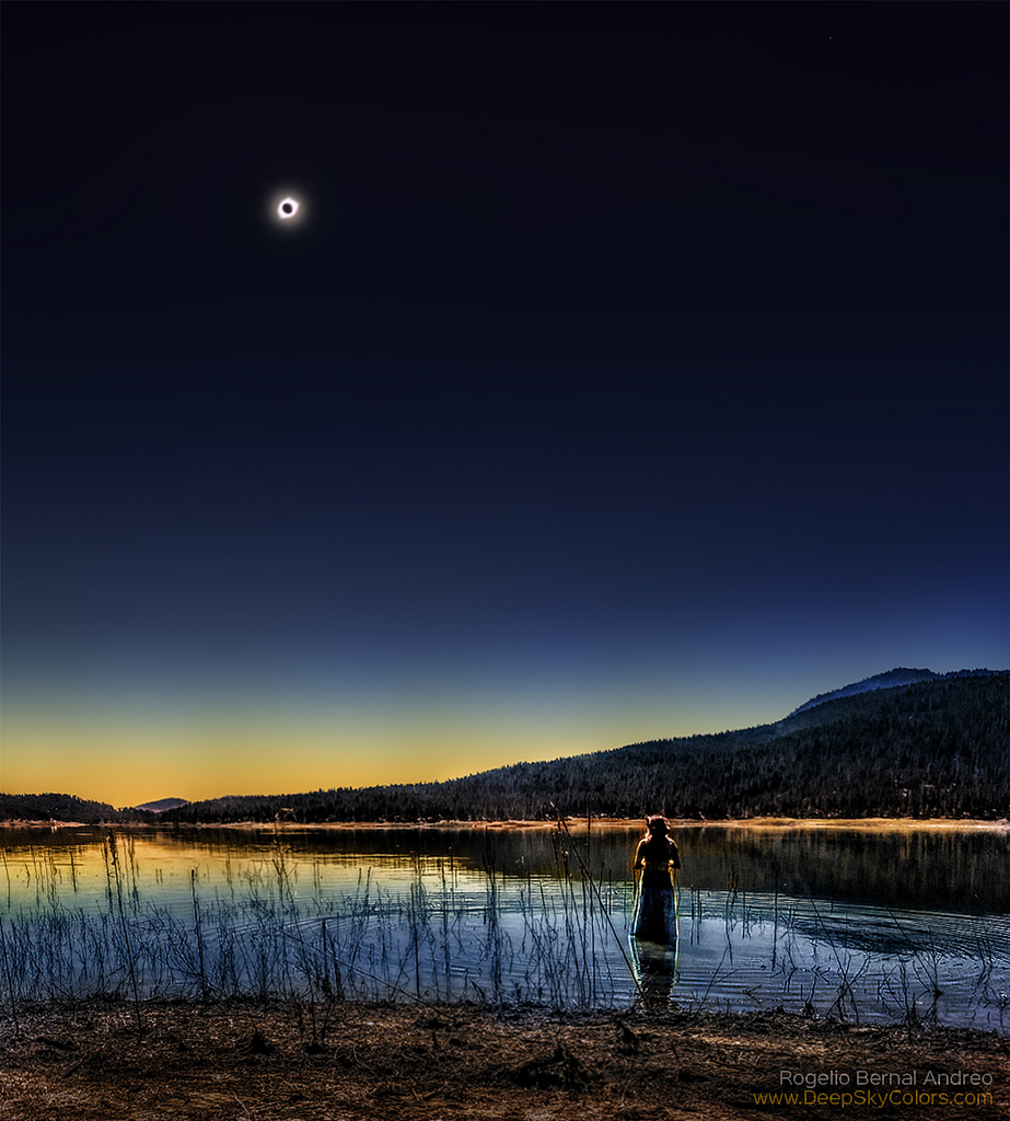 Sonnenfinsternis in den USA: Hinter einem See und einem bewaldeten Berg leuchtet am dunklen Himmel die Korona der Sonne um den Mond herum.