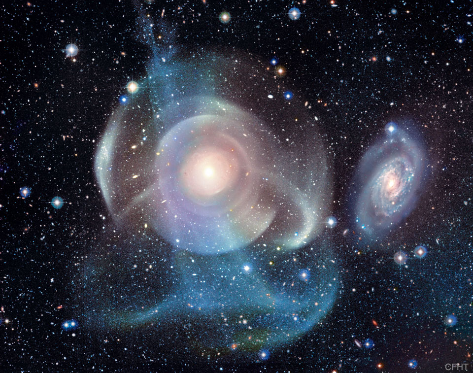 Die Galaxie mitten im Bild ist von eigentümlichen Schalen umgeben. Rechts daneben ist eine kleinere Galaxie, die eher gewöhnlich aussieht. Im Vordergrund sind unterschiedlich große Sterne verteilt.