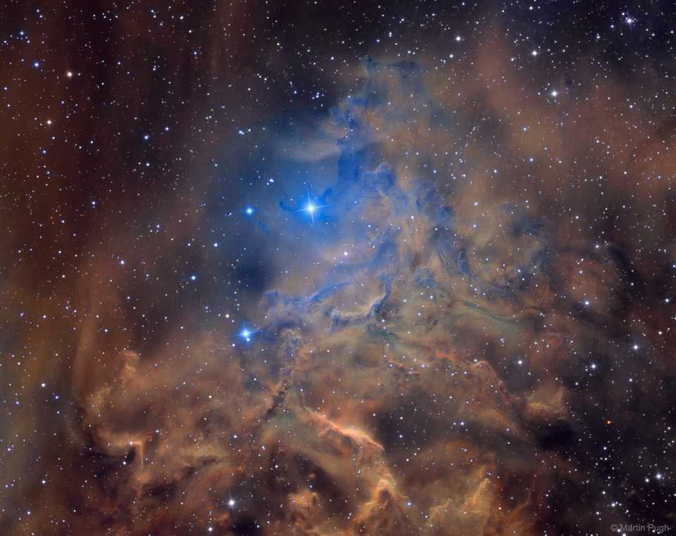 In einer Umgebung von braun leuchtenden Nebeln schimmert hinten wie durch eine Öffnung ein blauer Nebel mit einem helleren Stern in der Mitte hervor.