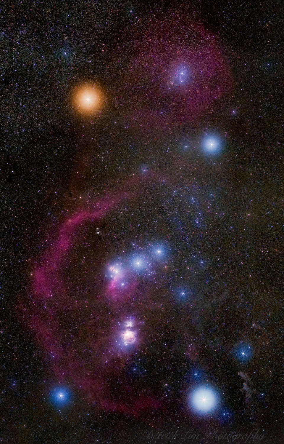 Die Sterne des Orion sind von bunten Schleiern umgeben. Man sieht auch die Barnardschleife, den Orionnebel und einige weitere Details.
