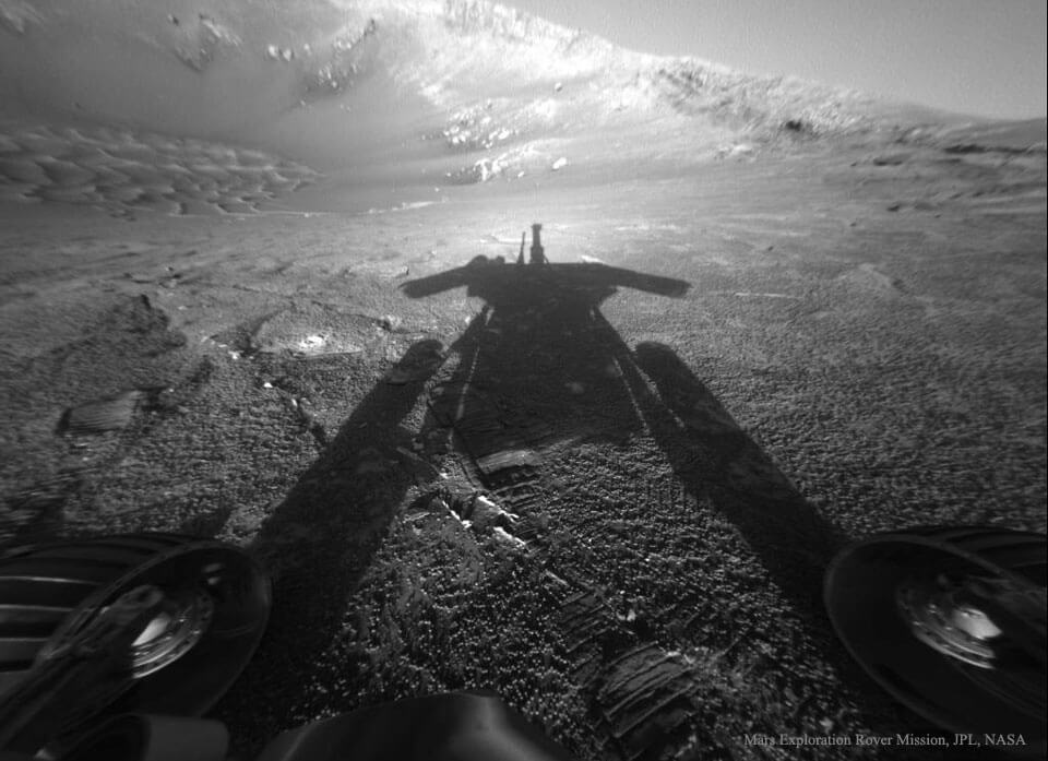 Der Marsrover Opportunity blickt in Gegenrichtung der Sonne und sieht seinen Schatten. Hinten ist der Rand des Kraters Endurance, vorne sieht man zwei Räder des Rovers.