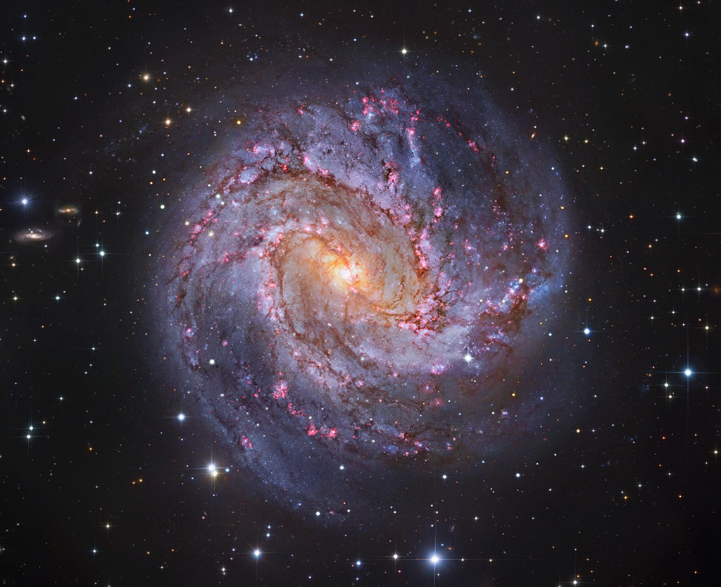 Die Spiralgalaxie M83 im Bild hat prachtvolle Spiralarme. Ihr gelblicher Kern ist von blau und rot leuchtenden Sternhaufen und Sternbildungsgebieten gesprenkelt.
