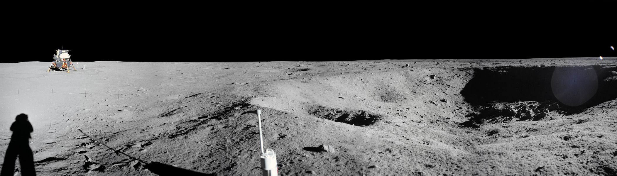 Links über dem Schatten des Astronauten Neil Armstrong steht das Landemodul von Apollo 11. Rechts ist ein großer Krater.