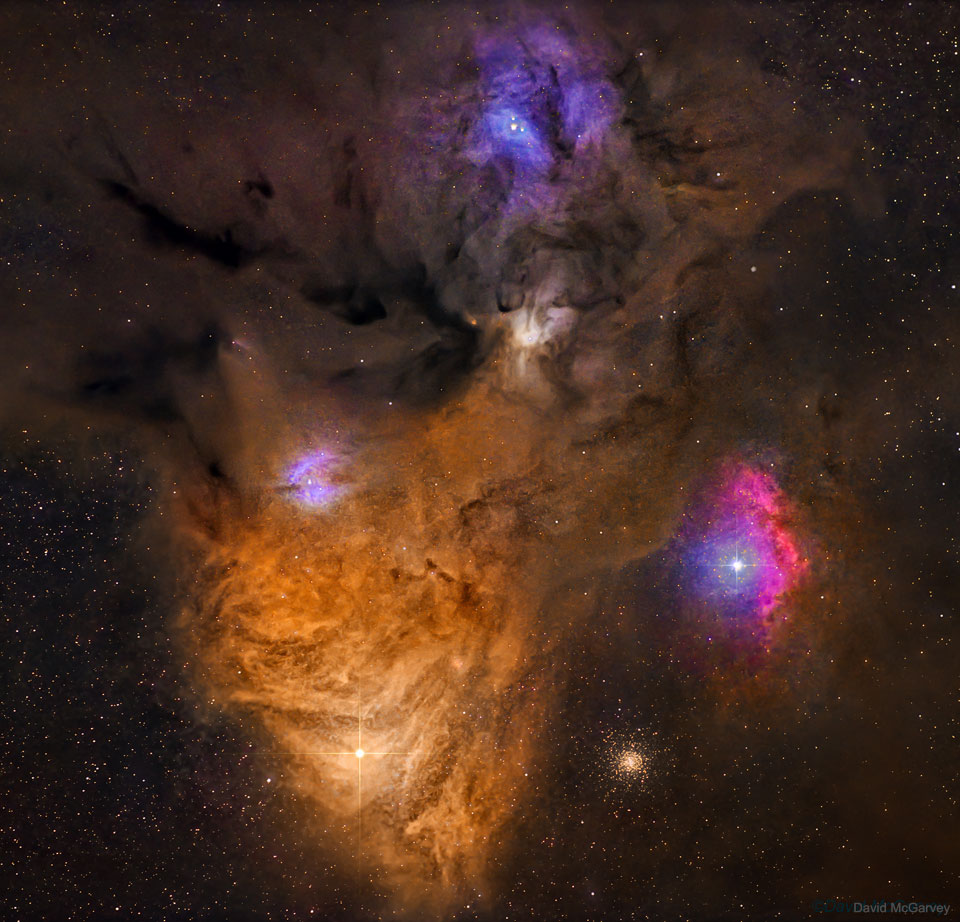Das Bild zeigt sehr farbenprächtige Wolken, unten bis zur Mitte ein orangegelber, stark strukturierter Nebel, dazu einige violette kleine Nebel um Sterne. Rechts unten ist ei Sternhaufen.