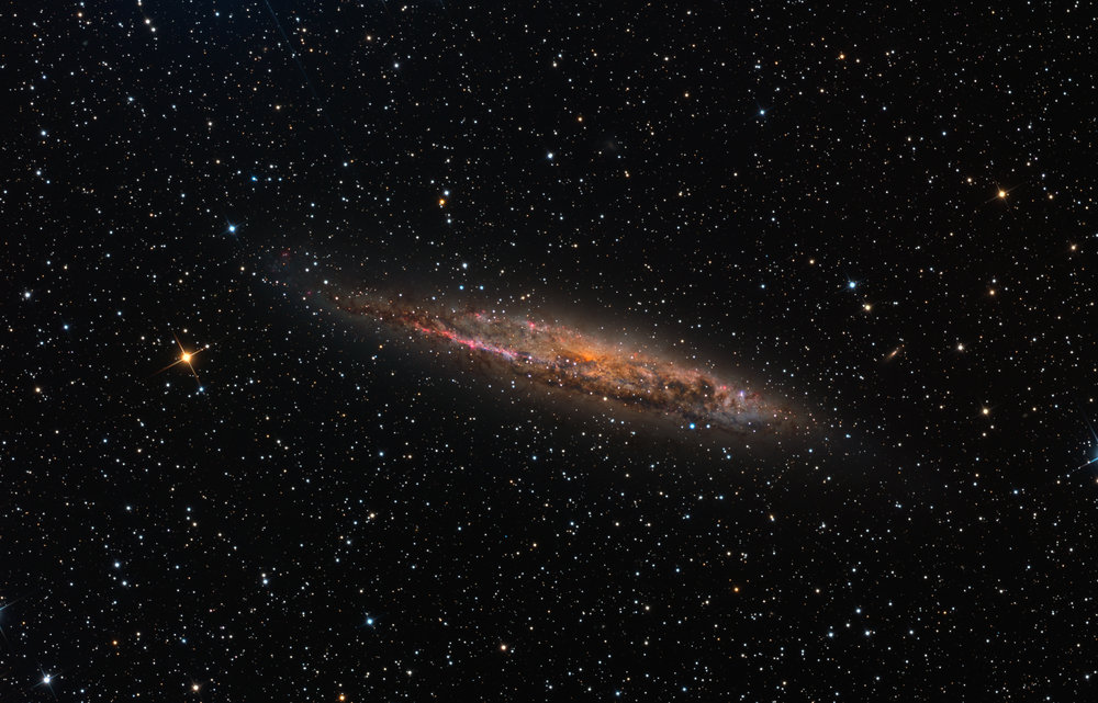 Mitten im sternklaren Bild ist eine nicht allzu groß gezeigte unregelmäßige Galaxie von der Seite zu sehen.