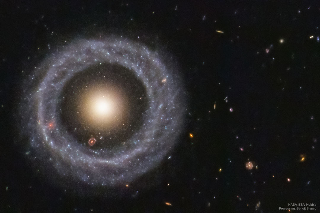 Eine Galaxie, die aus einem hellen Kern besteht, darum herum eine Leere, an die ein Sternenring anschließt. Durch die Lücke sieht man eine zweite, ähnich geformte Galaxie.