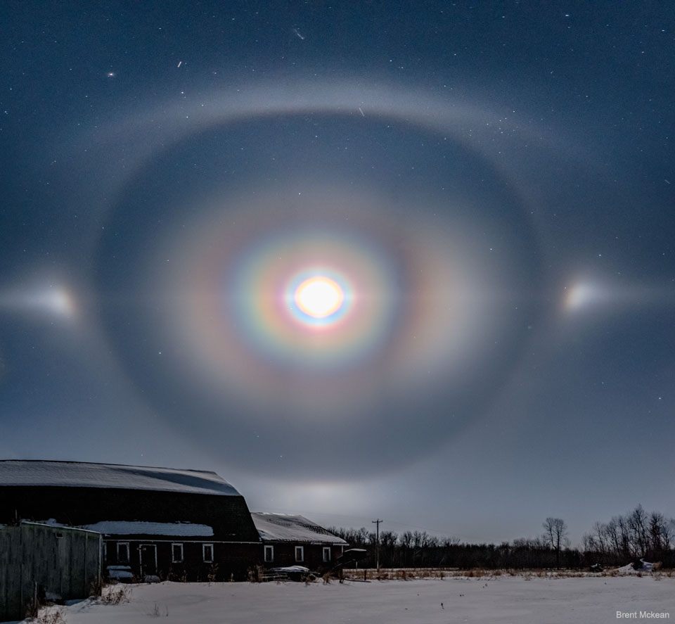 Mond mit Korona, 22-Grad-Halo und Bögen über Manitoba in Kanada. Der Mond wirkt, als wäre er von vielen Regenbögen umgeben.