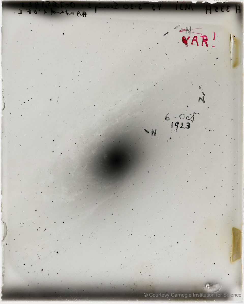 In der Mitte einer alten Fotoplatte ist ein schwarzer, unscharfer Fleck, es ist eine negative Abbildung der Andromeda-Galaxie, rechts oben ist mit roter Tinte "VAR!" notiert.