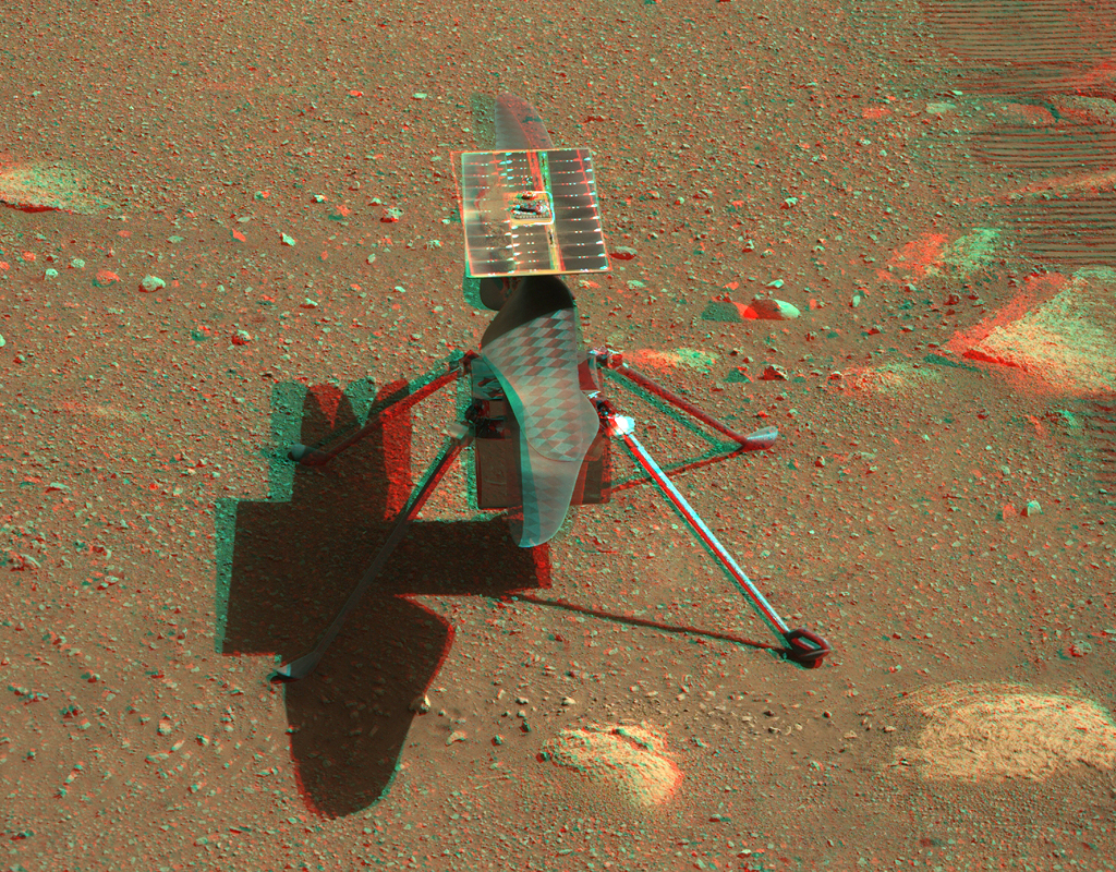Der Mars-Helikopter Ingenuity steht neben den Radspuren des Rovers Perseverance und wirft seinen Schatten auf die Marsoberfläche.