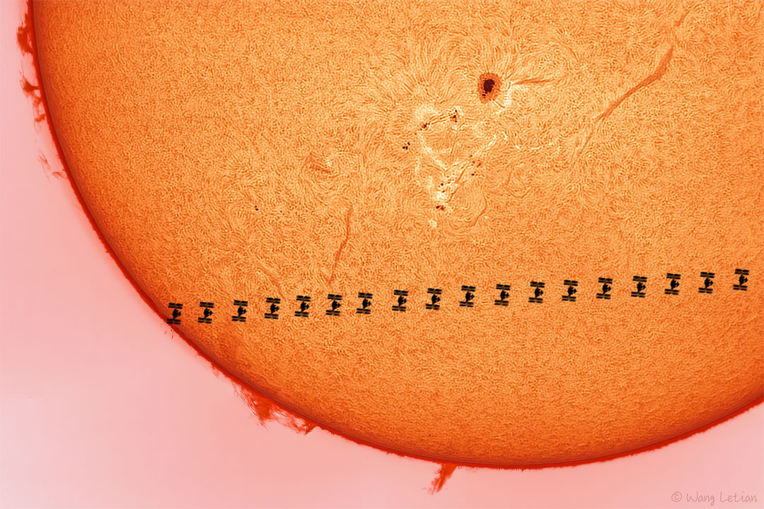 Das Bild zeigt eine Zeitraffer-Silhouette der Internationalen Raumstation (ISS), die über die Sonne zieht. Die Sonne zeigt Filamente, Protuberanzen und einen Sonnenfleck.