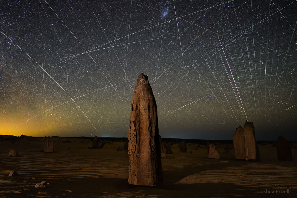 Das Bild zeigt die als Pinnacles bekannten Felsspitzen in Australien. Hinter den Türmen ist ein Himmel voller Satellitenspuren, viele stammen von der Starlink-Satellitenkonstellation im erdnahen Orbit.