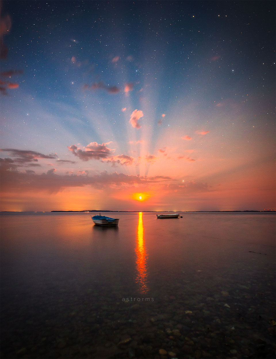 Das Bild zeigt den Mond, der über Wasser aufgeht, umgeben von hellen Strahlen, die durch die Wolken dringen.