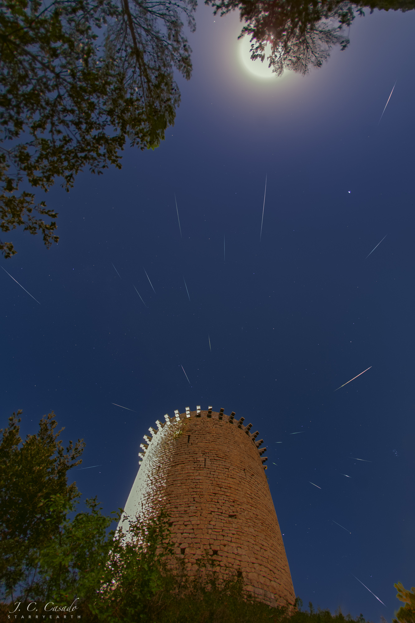 Hinter einem mittelalterlichen Turm in Sant Llorenç de la Muga in der spanischen Provinz Girona befindet sich der Radiant des Meteorstroms der Perseiden, oben leuchten der Vollmond und der Planet Saturn.