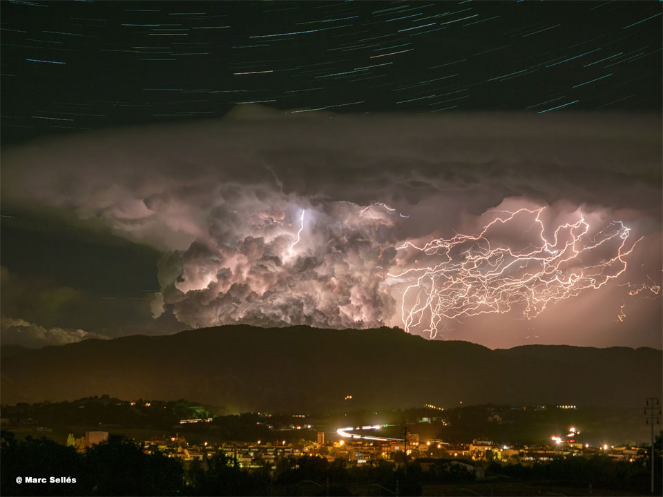 Komplexe, verworrene Blitze zucken über dem Serra de Bellmut in den Pyrenäen, dahinter leuchten die Strichspuren von Sternen.
