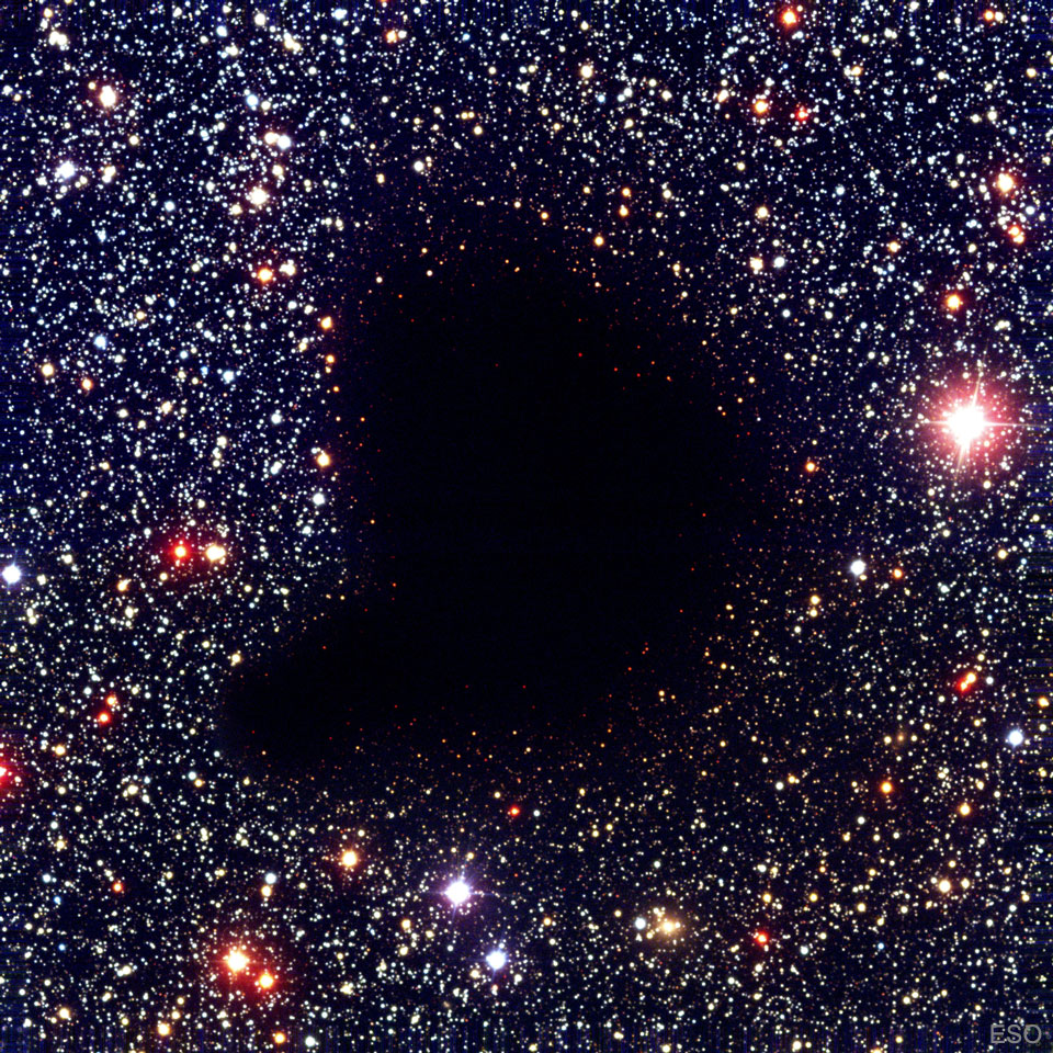 Die dunkle Molekülwolke Barnard 68 sieht aus wie ein Loch im Himmel inmitten vieler Sterne. Beschreibung im Text.
