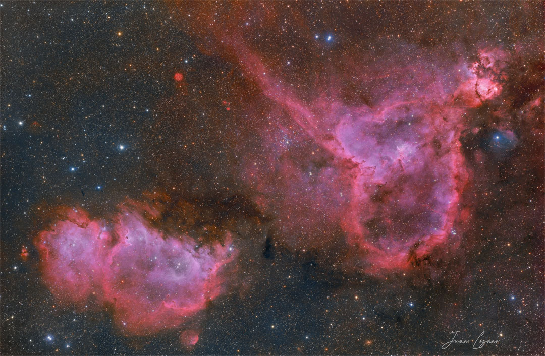 Zwei rote Emissionsnebel liegen vor einem dunklen aber farbenreichen Sternenfeld. Der Seelennebel befindet sich links unten, der Herznebel ist rechts oben.