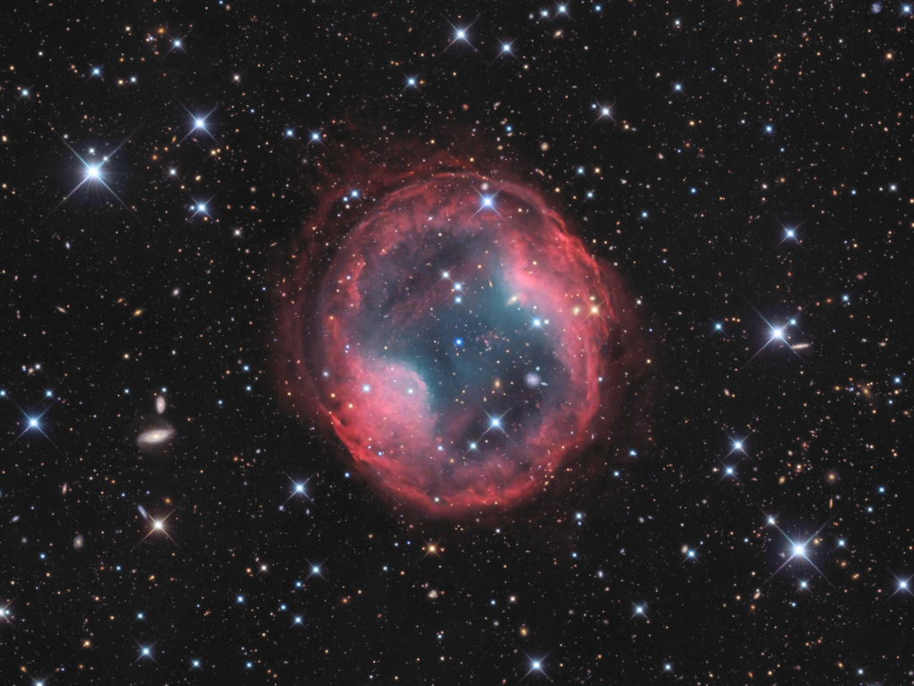 Der Planetarische Nebel Jones-Emberson 1 ist hier mit rötlicher Außenhülle abgeildet, im Zentrum ist ein weißer Zwergstern zu sehen.