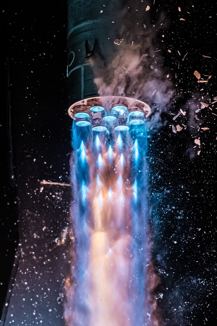 Aus 9 Raketendüsen strömt blaues Licht und breitet sich nach unten zu einem Abgasstrahl aus. Im Bild fallen Eistrümmer zu Boden.
