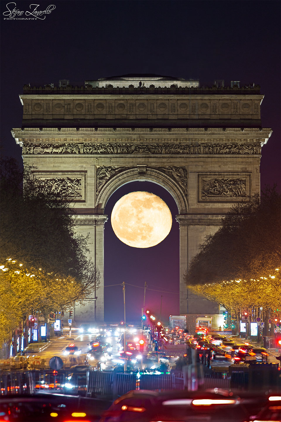 Hinter dem Triumphbogen in Paris leuchtet der Mond genau im oberen Teil des Bogens eingepasst.