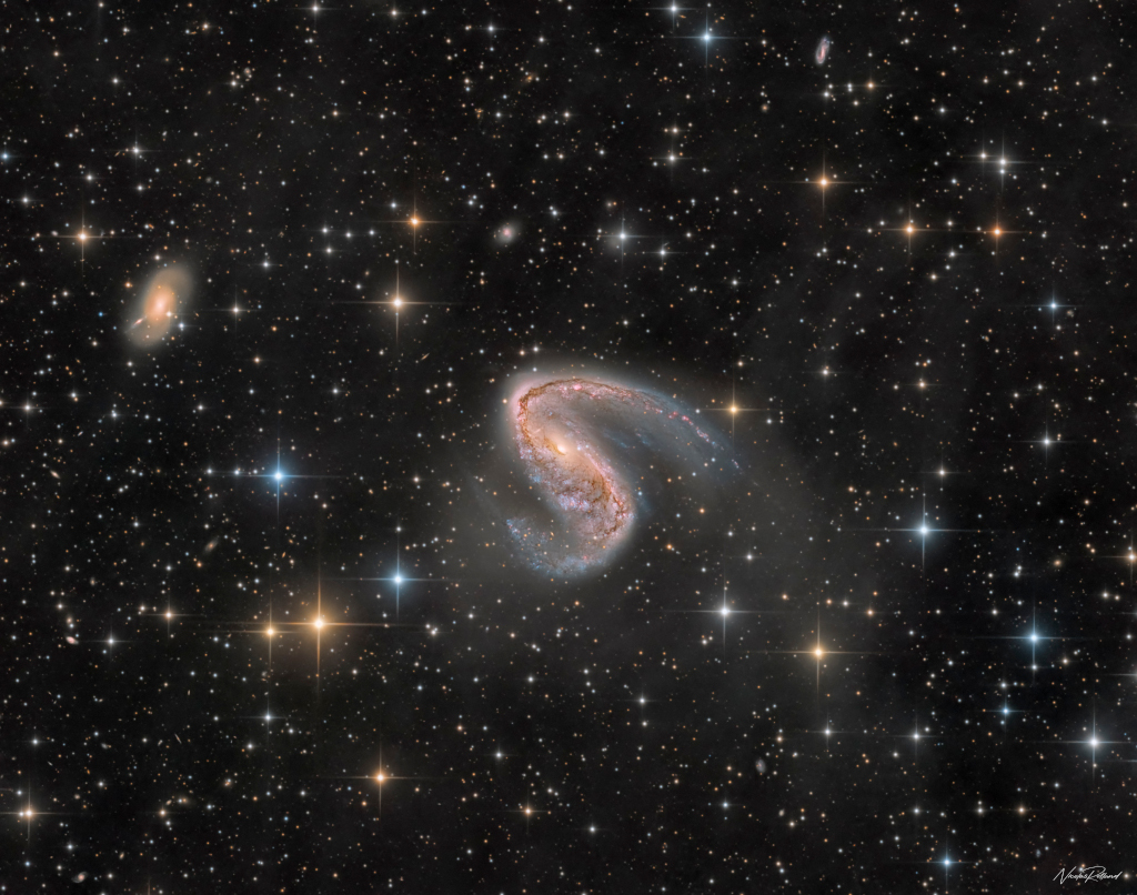 Im Bildfeld mit lose verstreuten, gezackten Sternen liegt in der Mitte eine S-förmige Balkenspiralgalaxie, links daneben eine kleinere, elliptisch wirkende Galaxie.