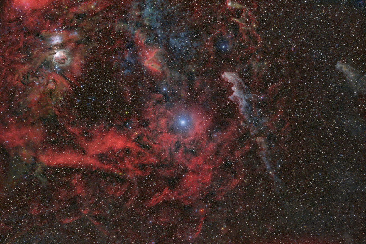 Im weiten Stern- und Nebelfeld leuchtet links oben der Orionnebel, um den Stern Rigel in der Mitte ist ein rötlicher Nebel angeordnet, und rechts daneben befindet sich der Hexenkopfnebel.