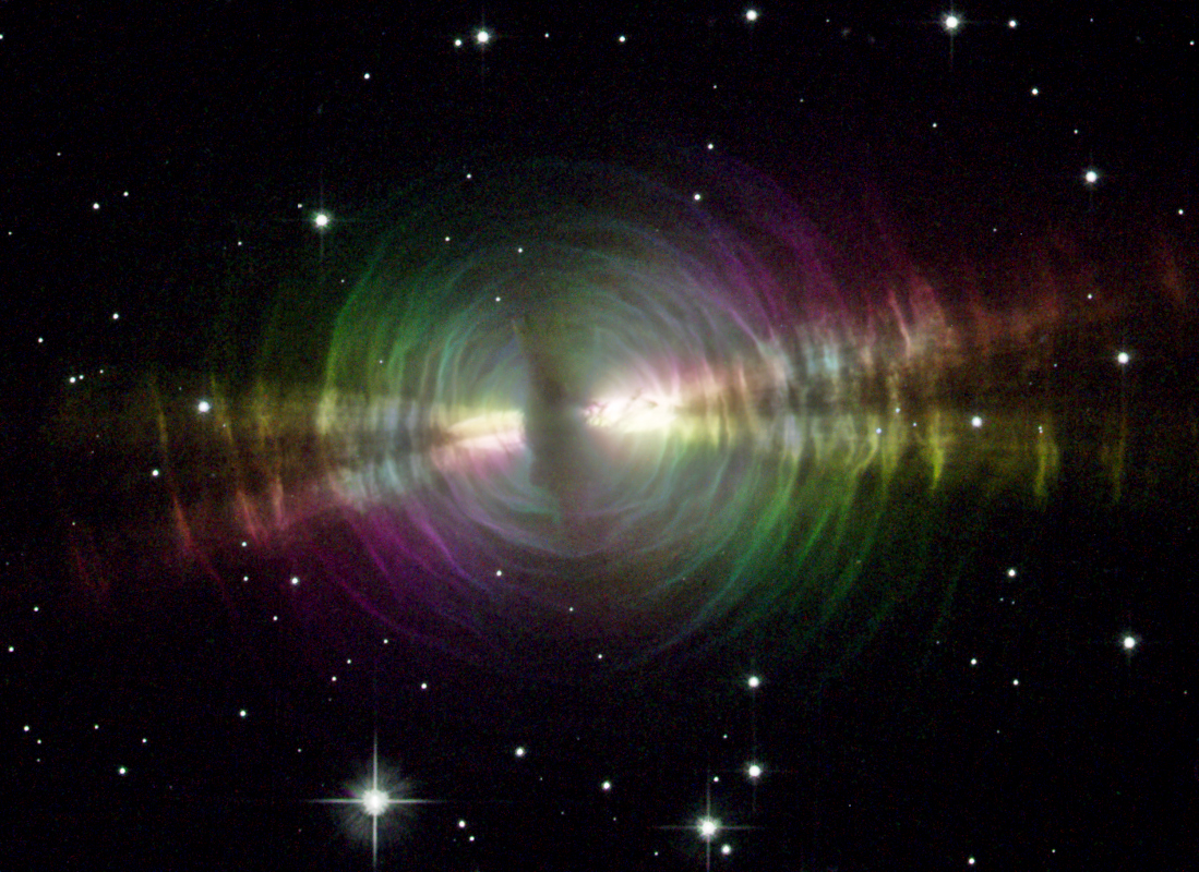 Um eine dunkle Staubstelle, hinter der sich ein alternder Stern verbirgt, sind konzentrische Nebelhüllen angeordnet. In der Mitte ist eine horizontale X-Struktur erkennbar.