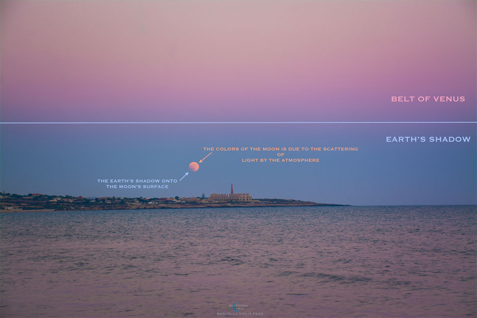 Der Himmel über Sizilien bei Sonnenuntergang zeigt von oben nach unten ein rosafarbenes Band, ein blaues Band, in dem der Mond leuchtet, das Festland mit einem Gebäude und Wasser, in dem sich das rosafarbene und das blaue Band spiegeln.